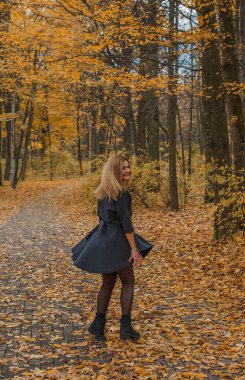 Sonbaharda parkta yürüyen Avrupa ve Ortadoğu görünümlü modern bir kadın. Şık mevsimlik kıyafetler, ılık ışık ve sonbahar renkleri rahat bir yaşam tarzı yaratıyor..
