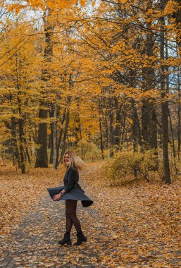 Sonbaharda parkta yürüyen Avrupa ve Ortadoğu görünümlü modern bir kadın. Şık mevsimlik kıyafetler, ılık ışık ve sonbahar renkleri rahat bir yaşam tarzı yaratıyor..