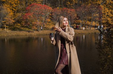 Sonbaharda parkta yürüyen Avrupa ve Ortadoğu görünümlü modern bir kadın. Şık mevsimlik kıyafetler, ılık ışık ve sonbahar renkleri rahat bir yaşam tarzı yaratıyor..