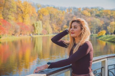 Sonbaharda parkta yürüyen Avrupa ve Ortadoğu görünümlü modern bir kadın. Şık mevsimlik kıyafetler, ılık ışık ve sonbahar renkleri rahat bir yaşam tarzı yaratıyor..