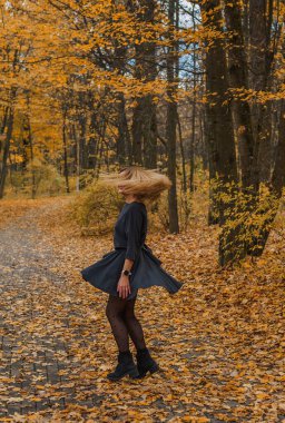 Sonbaharda parkta yürüyen Avrupa ve Ortadoğu görünümlü modern bir kadın. Şık mevsimlik kıyafetler, ılık ışık ve sonbahar renkleri rahat bir yaşam tarzı yaratıyor..