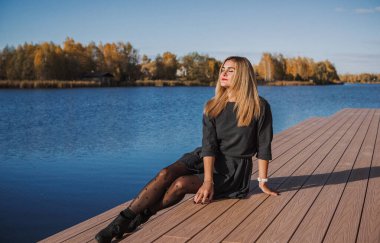 Sonbaharda parkta yürüyen Avrupa ve Ortadoğu görünümlü modern bir kadın. Şık mevsimlik kıyafetler, ılık ışık ve sonbahar renkleri rahat bir yaşam tarzı yaratıyor..