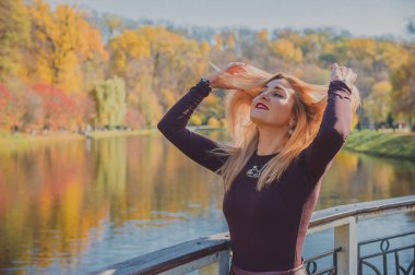 Sonbaharda parkta yürüyen Avrupa ve Ortadoğu görünümlü modern bir kadın. Şık mevsimlik kıyafetler, ılık ışık ve sonbahar renkleri rahat bir yaşam tarzı yaratıyor..