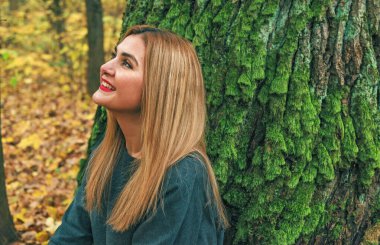 Sonbaharda parkta yürüyen Avrupa ve Ortadoğu görünümlü modern bir kadın. Şık mevsimlik kıyafetler, ılık ışık ve sonbahar renkleri rahat bir yaşam tarzı yaratıyor..