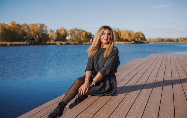 Sonbaharda parkta yürüyen Avrupa ve Ortadoğu görünümlü modern bir kadın. Şık mevsimlik kıyafetler, ılık ışık ve sonbahar renkleri rahat bir yaşam tarzı yaratıyor..