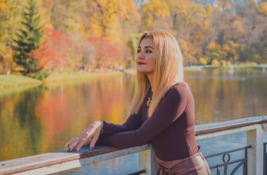 Sonbaharda parkta yürüyen Avrupa ve Ortadoğu görünümlü modern bir kadın. Şık mevsimlik kıyafetler, ılık ışık ve sonbahar renkleri rahat bir yaşam tarzı yaratıyor..