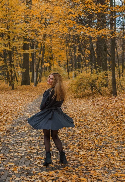 Sonbaharda parkta yürüyen Avrupa ve Ortadoğu görünümlü modern bir kadın. Şık mevsimlik kıyafetler, ılık ışık ve sonbahar renkleri rahat bir yaşam tarzı yaratıyor..