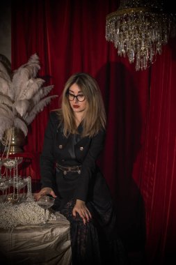 Siyah takım elbiseli ve kedi gözü gözlüklü zarif olgun bir kadın. Kırmızı arka planda entelektüel ve çekici bayan