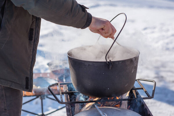 Outdoor winter cooking, man preparing food in cauldron