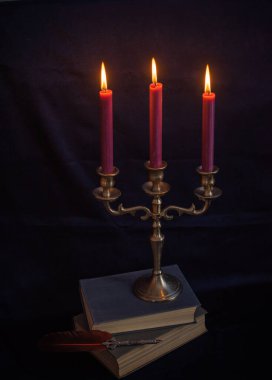 Zarif antika bronz mum tutacağı ve koyu mavi arka planda yumuşak bir şekilde parlayan üç tane burgundy mumu. Metalin dokusunu ve detaylarını vurgulayan klasik, minimalist kompozisyon