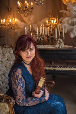 Karanlık Vintage Interior 'daki Baş Rahibe. 50 yaşında, kızıl saçlı, gizemli bakışlı zarif mavi dantelli elbisesi olan çekici bir kadının çarpıcı portresi.