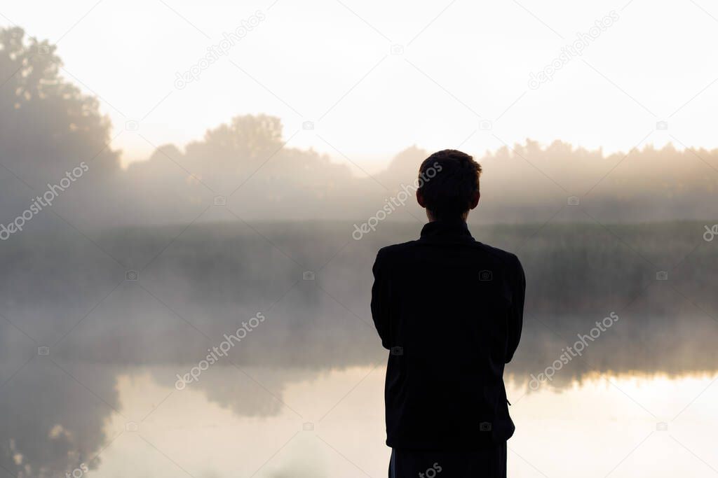 Man standing alone looking out to the pond. Moment before sunrise