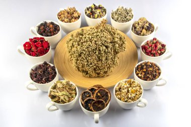 Beyaz arka planda fincanlarda çeşitli bitkisel çay malzemeleri var. Doğal bitkiler ilacı..