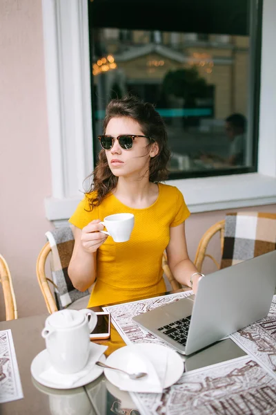 Молодая красивая девушка с ноутбуком и чаем в кафе на открытом воздухе — стоковое фото