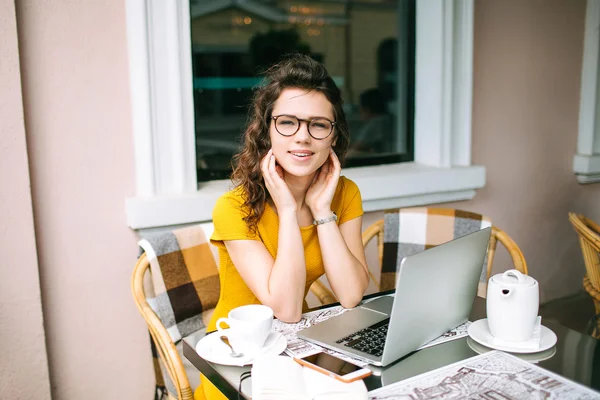 Девушка в очках с ноутбуком и чаем в кафе на открытом воздухе — стоковое фото
