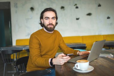 Dizüstü bilgisayar, akıllı telefon ve kahve kafede çalışan genç yenilikçi