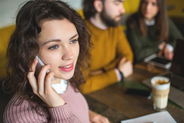 Молодая женщина разговаривает по телефону со счастливыми друзьями в кафе — стоковое фото