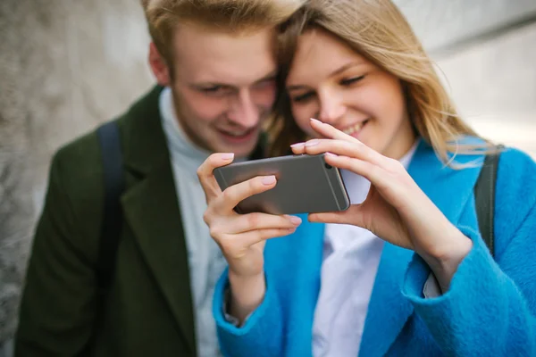 Joven rubia hombre y mujer mirando en el teléfono inteligente y sonriendo — Foto de Stock