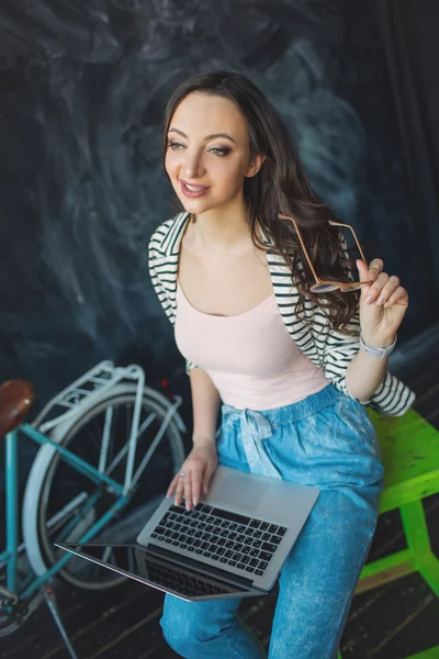 Joven mujer bonita con el ordenador portátil de rodillas en el estudio con bicicleta — Foto de Stock