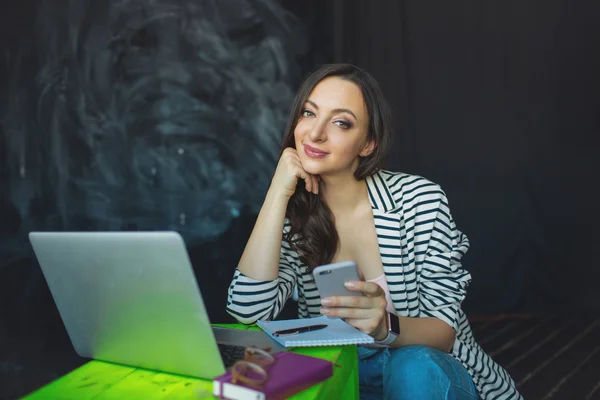 Молодая красивая женщина с ноутбуком и смартфоном в помещении — стоковое фото