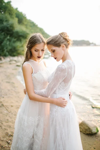 Hermanas gemelas en vestido de novia en la orilla del mar —  Fotos de Stock