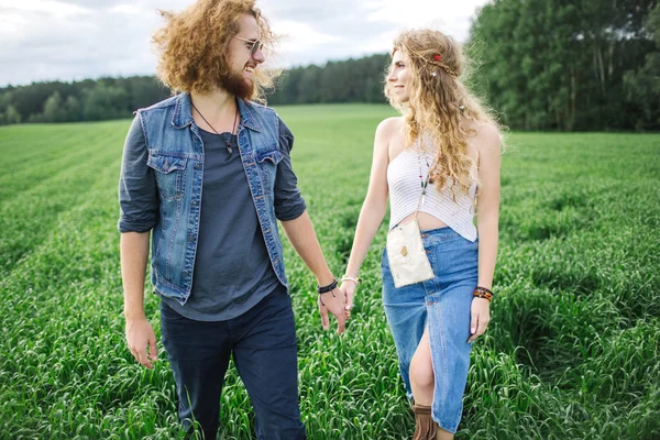 Jovem casal hippie bonito andando no campo de verão verde — Fotografia de Stock