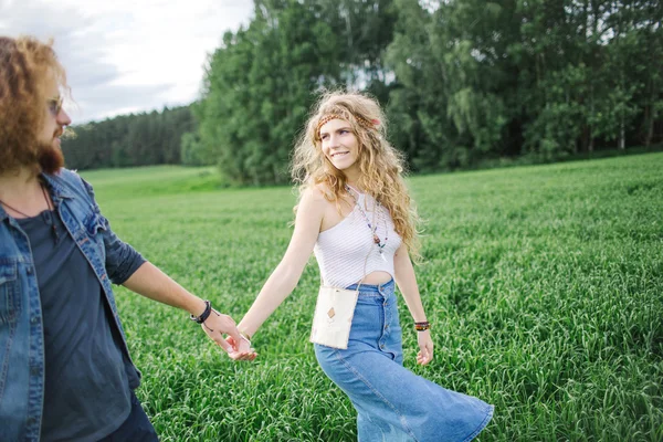 Jovem casal hippie bonito andando no campo de verão verde — Fotografia de Stock