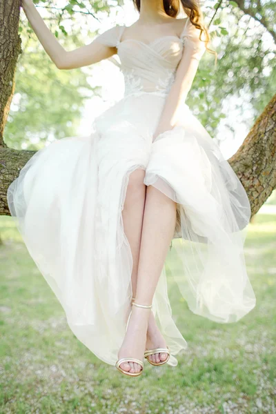 Novia joven en hermoso vestido de novia sentado en el árbol al aire libre —  Fotos de Stock