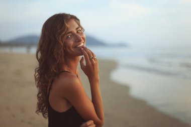 Akşam güneşin altında deniz kenarında uzun kıvırcık saçlı genç güzel kadın