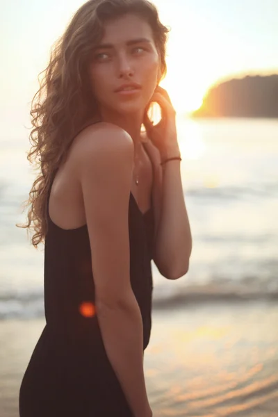 Jovem mulher bonita com cabelos longos encaracolados à beira-mar sob o pôr do sol da noite — Fotografia de Stock