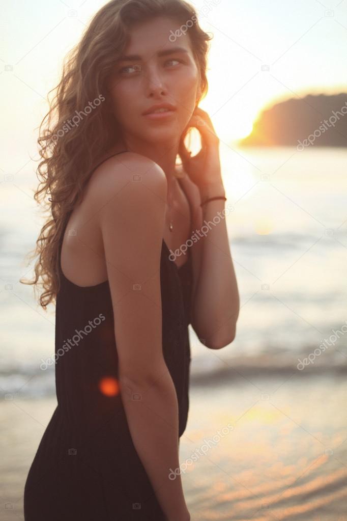 Young beautiful woman with long curly hair at the seaside under the evening sunset