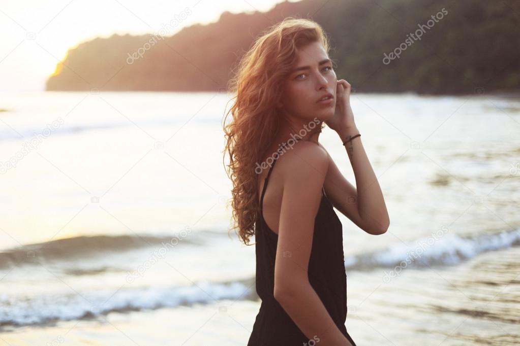 Young beautiful woman with long curly hair at the seaside under the evening sunset