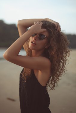 Akşam güneşin altında deniz kenarında uzun kıvırcık saçlı genç güzel kadın