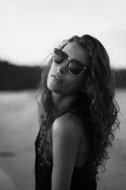 Akşam güneşin altında deniz kenarında uzun kıvırcık saçlı genç güzel kadın