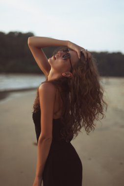 Akşam güneşin altında deniz kenarında uzun kıvırcık saçlı genç güzel kadın