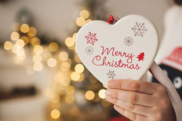 Juguete en forma de corazón de Navidad en manos de mujer sobre fondo de árbol de Navidad — Foto de Stock