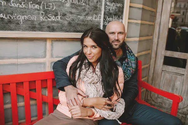 Giovane coppia seduta alla panchina rossa vicino al caffè in città — Foto Stock