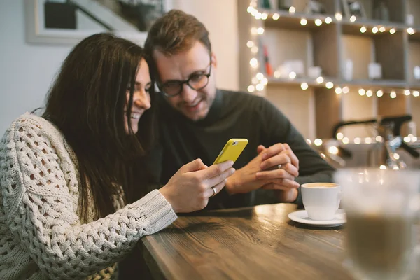 Молодая пара в кафе сидит со смартфоном и кофе — стоковое фото