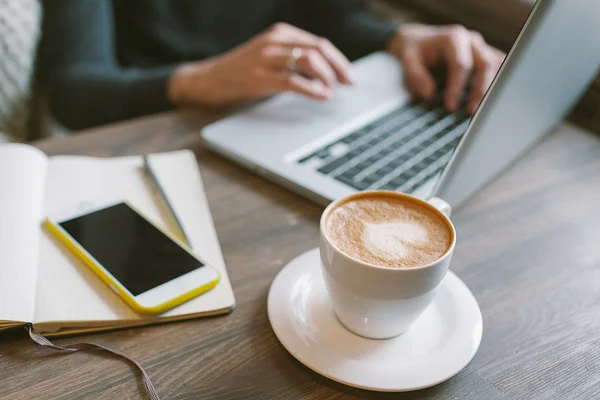 Manos del hombre en el ordenador portátil con café y smartphone con bloc de notas — Foto de Stock