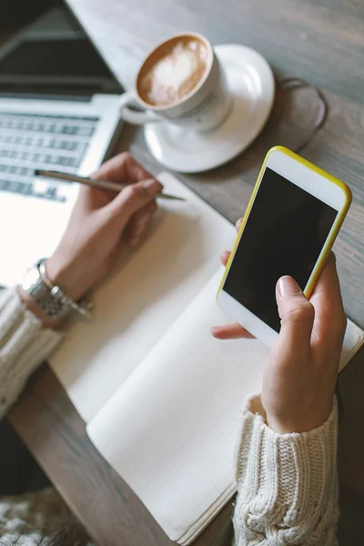 Manos de mujer con bolígrafo y bloc de notas, sosteniendo smartphone con cof —  Fotos de Stock