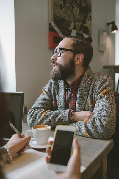 Hipster con barba con teléfono inteligente y portátil en la mesa ceder en — Foto de Stock