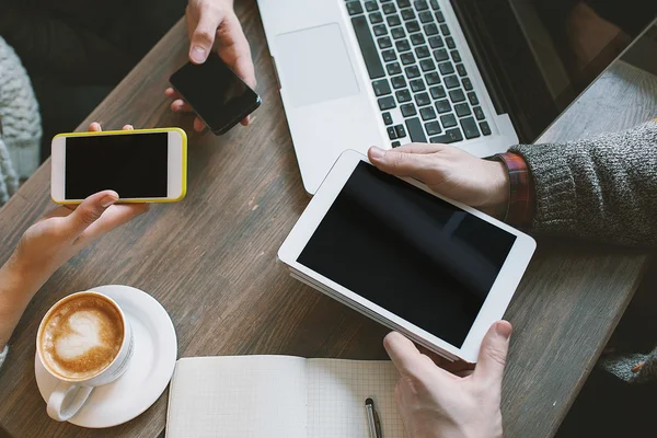 Handen met smartphones, tablet boven tafel met laptop en koffie — Stockfoto