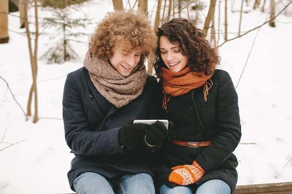 Casal segurando smartphone sentado ao ar livre no inverno — Fotografia de Stock