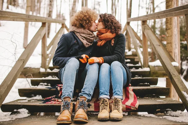 Young couple kissing on wooden stairs outdoors in winter — Stock Photo, Image