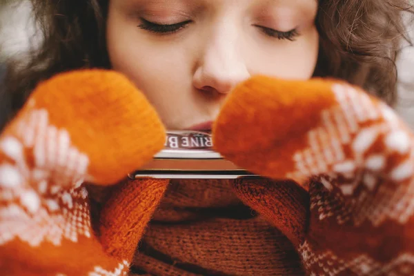 Mooi meisje met ogen gesloten spelen mondharmonica in winter handschoenen — Stockfoto