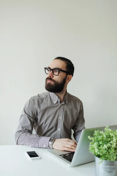 Hombre ocupado con barba en gafas pensando en el portátil y smartpho — Foto de Stock