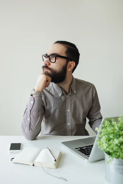 Hombre ocupado con barba en gafas pensando en el portátil y smartpho — Foto de Stock