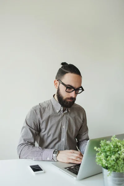 Man with beard in glasses typing laptop with smartphone — Stock Photo, Image