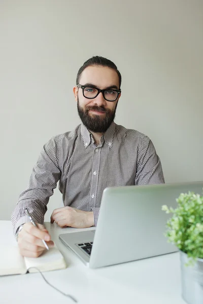 Hombre sonriente con barba en gafas tomando notas con portátil notep —  Fotos de Stock