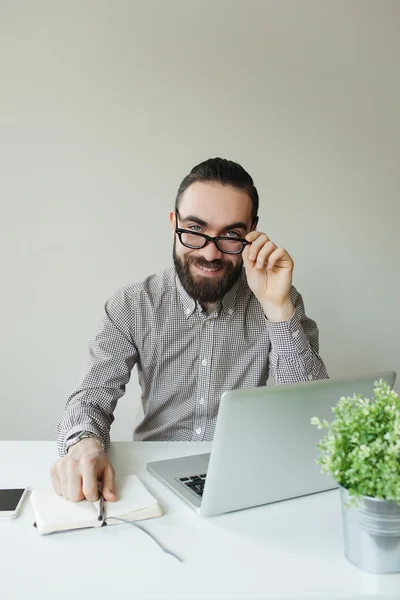 Homem sorridente com barba em óculos tomando notas com laptop notep — Fotografia de Stock